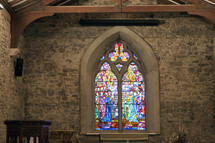 A stain glass window in a stone church sanctuary.