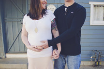 Expectant parents smiling and holding hands.
