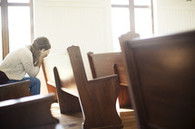 a woman hiding her face sitting in a church pew 