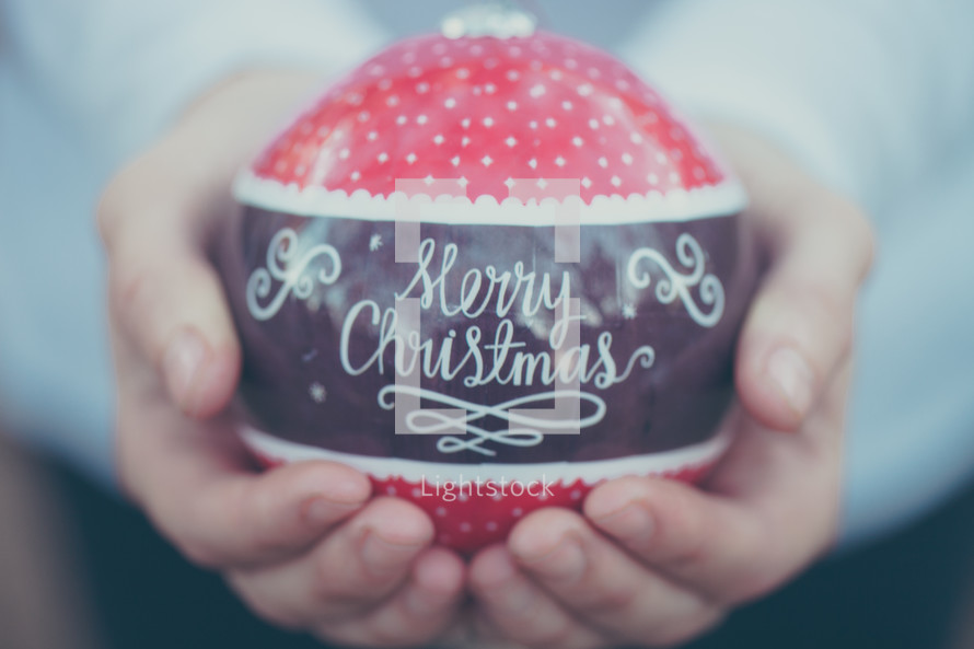 a large red ornament with the words Merry Christmas being held in someone's hands