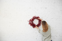 a woman standing with a red berry Christmas wreath 