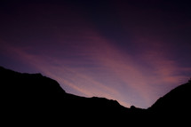 The sun sets over the mountain with purple and pink colors in the sky. 
