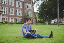 A man reads a Bible on a lawn outside an apartment building