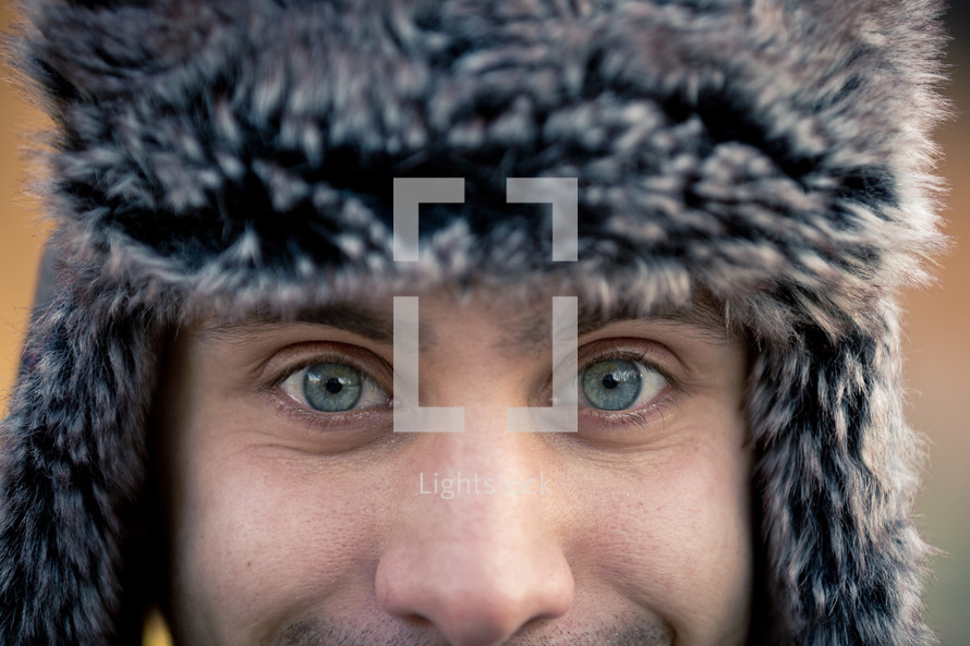 blue eyes of a man wearing a fur hunters hat