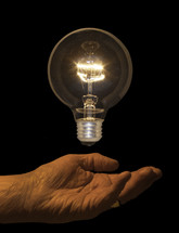 A shining light bulb floating above a person's hand.