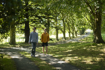 two young men walking and talking together on a driveway lined with trees in a beautiful setting