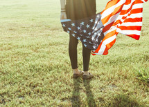a woman holding an American flag standing in grass 