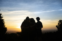 small group of  people standing together looking out over a valley at sunset