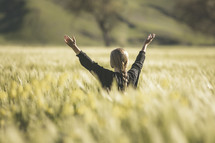 a woman standing in a field of wheat with raised arms 