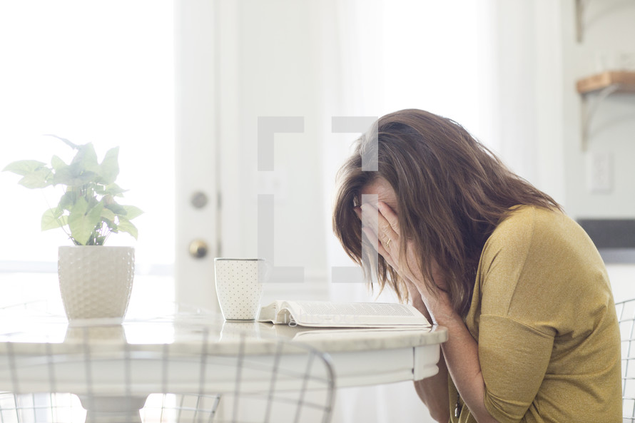 a woman crying with an open Bible on a kitchen table 