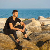 Portrait of a young man sitting on the rocks near the sea.