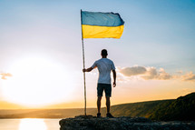 Happy ukrainian man with national flag on summer sky background on high rock. Patriot symbol. Free Ukraine. High quality photo