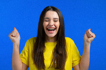 Woman is very glad and happy, she shows yes gesture of victory, she achieved result, goals. Surprised excited happy lady on blue studio background. Jackpot concept. High quality photo