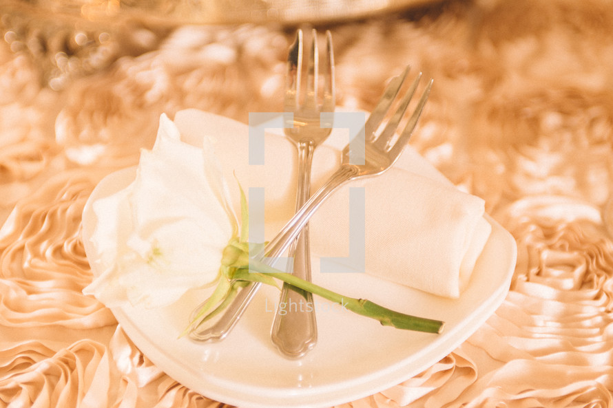 a rose, forks, and napkin on plates 