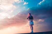 young woman standing on a ledge at sunset 