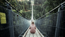 a woman sitting on a swinging bridge 