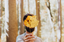 a man holding up a fall leaf in front of his face 