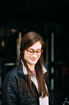 a woman wearing a coat and glasses looking down 