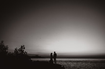 slhouette of a couple standing by a shore at dusk 