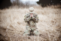 soldier kneeling in a field praying 