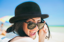 Portrait of smiling beautiful young woman in black hat retro sunglasses on beach. High quality photo