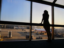 woman looking out airport windows at the terminal and runway 