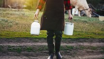 Woman walks through the countryside and carries two bottles milk after milking cow on farm pasture. Natural dairy products from farmer for healthy diet .Breeding cattle on village field. Natural food