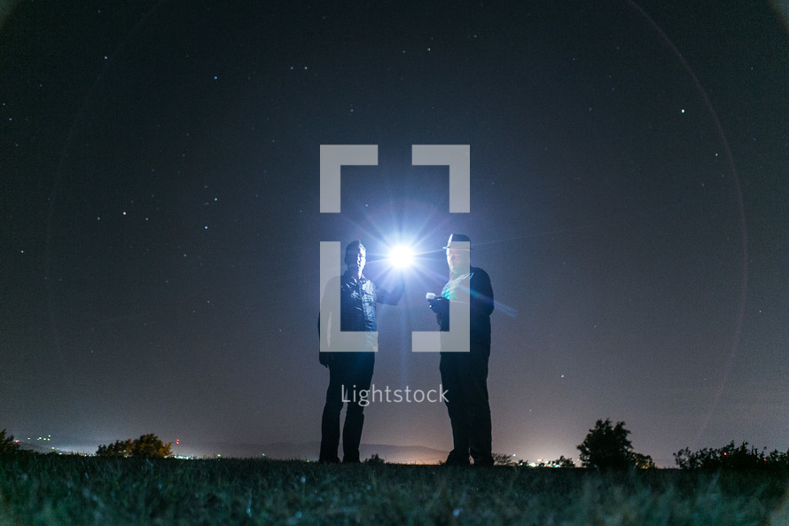 Men in park at night shining flashlight