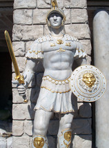 A life sized statue of a Roman guard with full battle armor, shield, sword and helmet adorned in gold accent to show the detail of what a roman soldier would look like during ancient Rome during the time of Christ. 