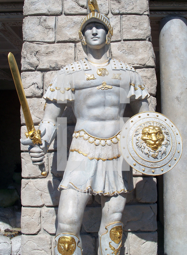 A life sized statue of a Roman guard with full battle armor, shield, sword and helmet adorned in gold accent to show the detail of what a roman soldier would look like during ancient Rome during the time of Christ. 
