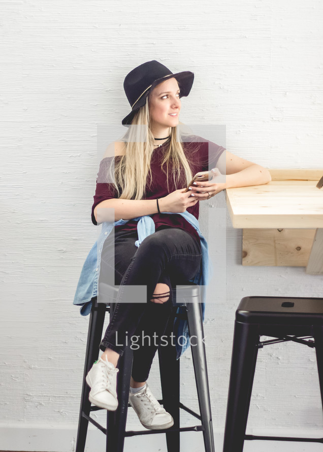 a young woman sitting on a stool holding a cellphone 