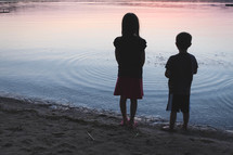 children standing in front of a lake at sunset 