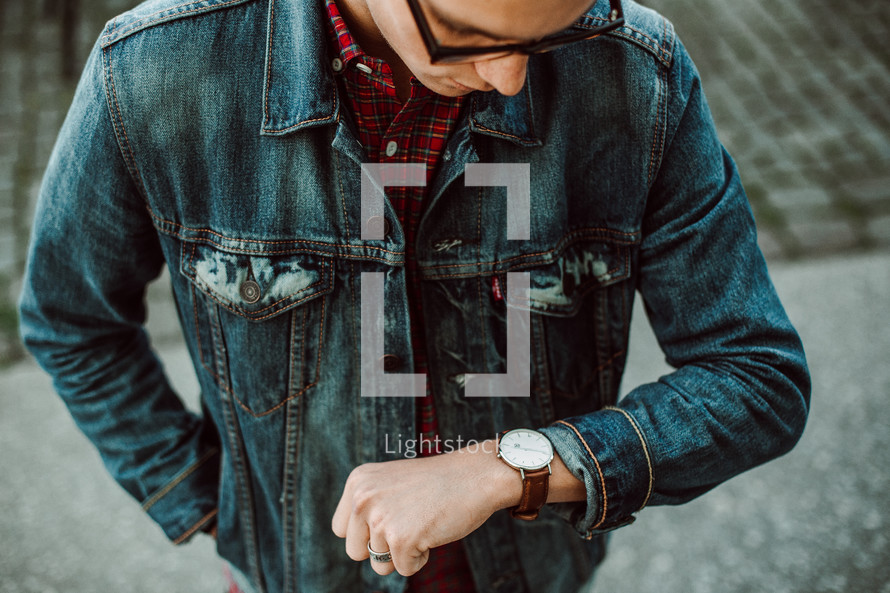 a young man in a jean jacket looking down at his watch 