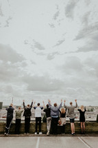 people standing on a rooftop parking deck with hands raised 