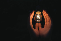 illuminated hands surrounding a light bulb