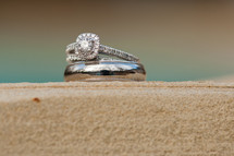 engagement ring and wedding band on sand
