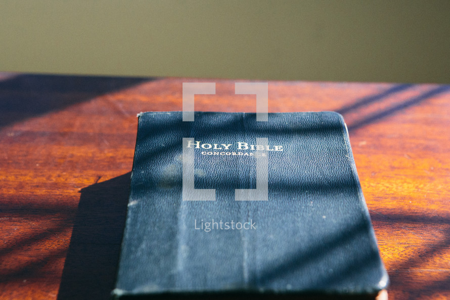 worn bible on wood table with light coming through window