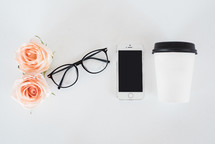roses, reading glasses, cellphone, and coffee cup on a white desk 