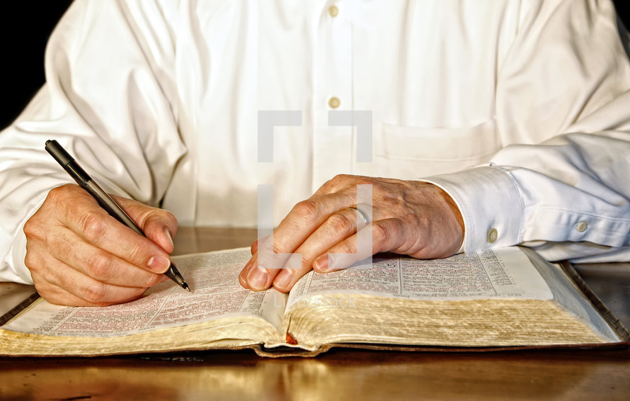 A businessman or business executive in a white, long-sleeved shirt takes time out of his day to study the Holy Bible.