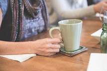 a woman sitting at a table with a mug of hot tea 