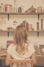 A woman sits at a desk with shelves on the wall.