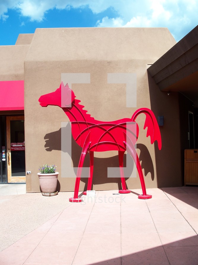 A sculpture of a red horse sits outside of an Arizona art gallery on a sunny day in the summertime. 