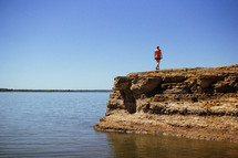 a woman walking along the edge of a cliff along a lake shore