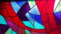 A colorful stained glass window with crimson red, violet, purple, aquamarine blue, navy blue and multiple colors in a church sanctuary window. 