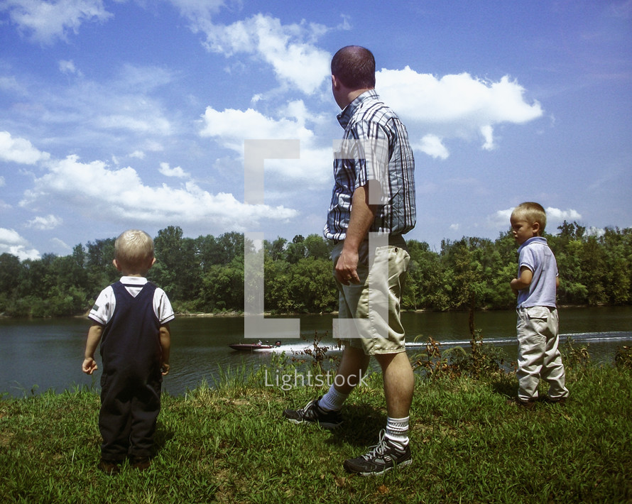father with his two sons standing near a lake 
