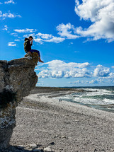a man sitting on a rocky shore near the ocean 