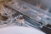 Close-up of silverware being washed in sink.