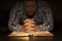 A man praying over an open Bible.