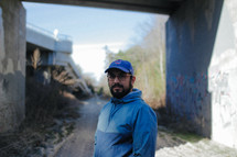 a man standing on a dirt road under a concrete overpass 