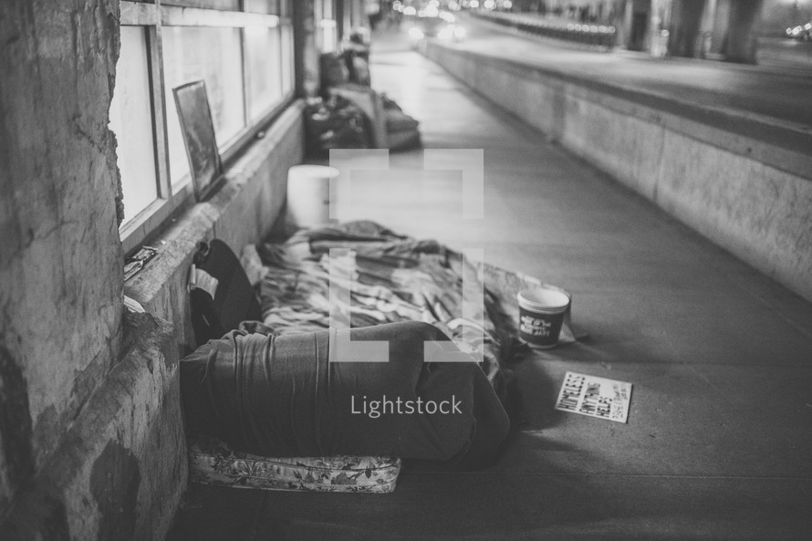 homeless sleeping bags on a city sidewalk at night 